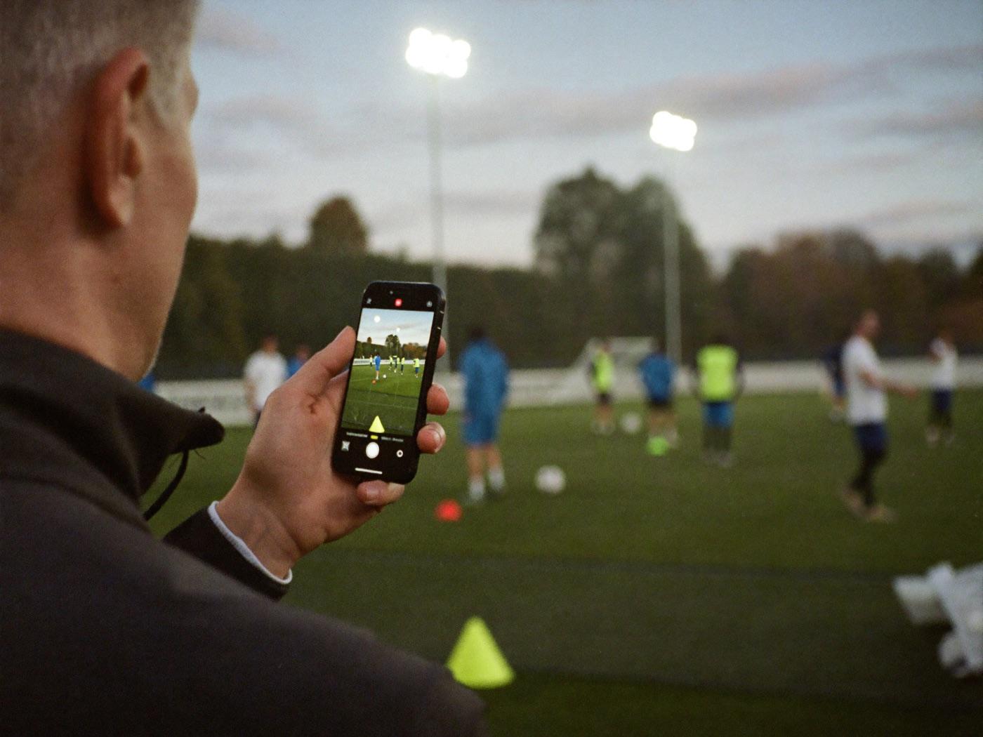 Trainer an der Seitenlinie mit dem Smartphone in der Hand